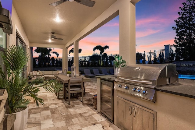 patio terrace at dusk featuring exterior kitchen, area for grilling, and ceiling fan