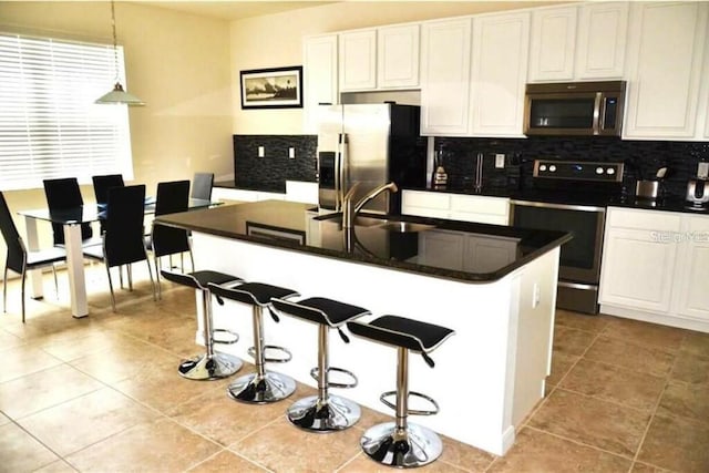 kitchen with a breakfast bar area, white cabinetry, stainless steel appliances, and decorative light fixtures