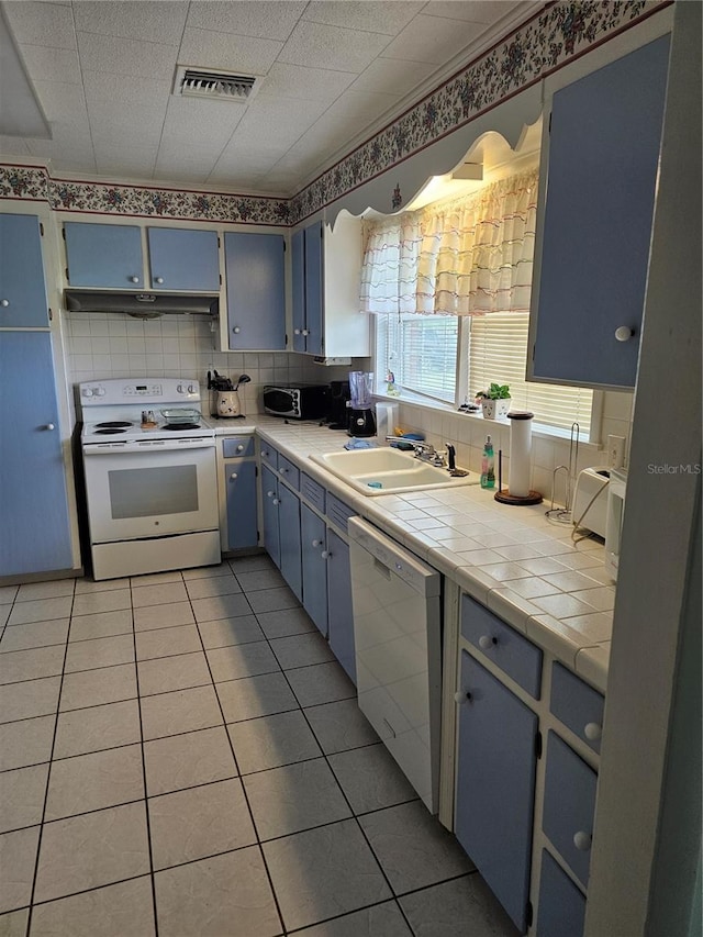 kitchen featuring backsplash, white appliances, sink, blue cabinetry, and tile counters