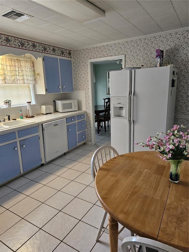 kitchen with light tile floors, blue cabinets, white appliances, backsplash, and sink