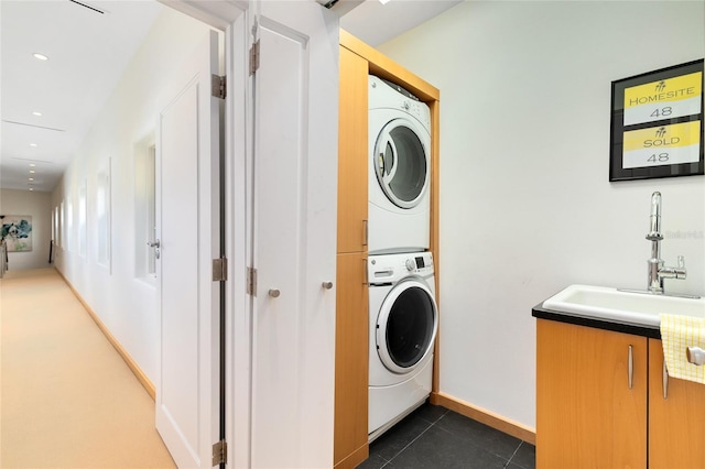 washroom with stacked washer and dryer, dark tile patterned floors, and sink