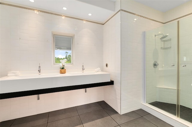 bathroom featuring a tile shower, tile patterned flooring, double sink, and tile walls