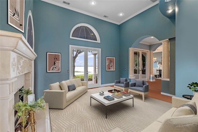 living room with a towering ceiling, decorative columns, a high end fireplace, ornamental molding, and french doors