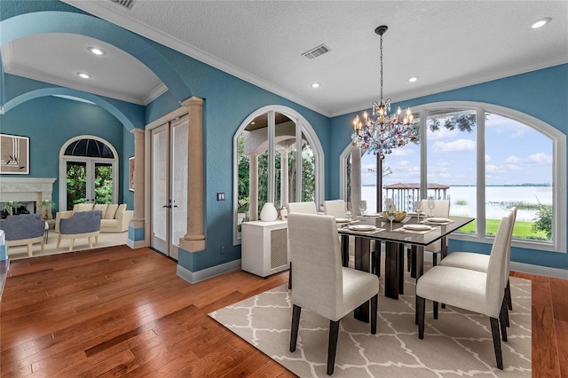 dining room with a water view, a textured ceiling, ornamental molding, a notable chandelier, and hardwood / wood-style floors