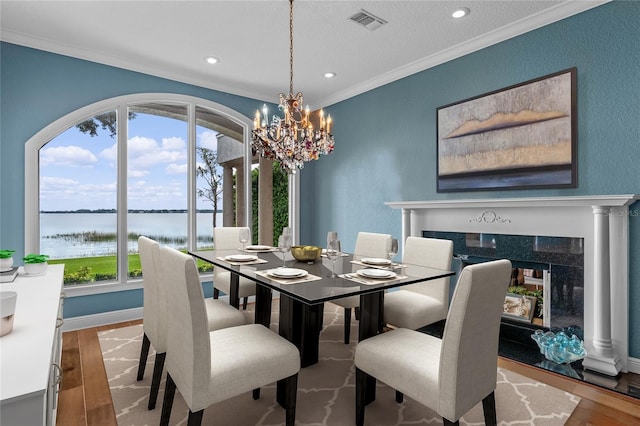 dining room with light hardwood / wood-style flooring, ornamental molding, a chandelier, and a water view