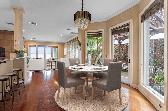 dining area with crown molding, a healthy amount of sunlight, wood-type flooring, and decorative columns