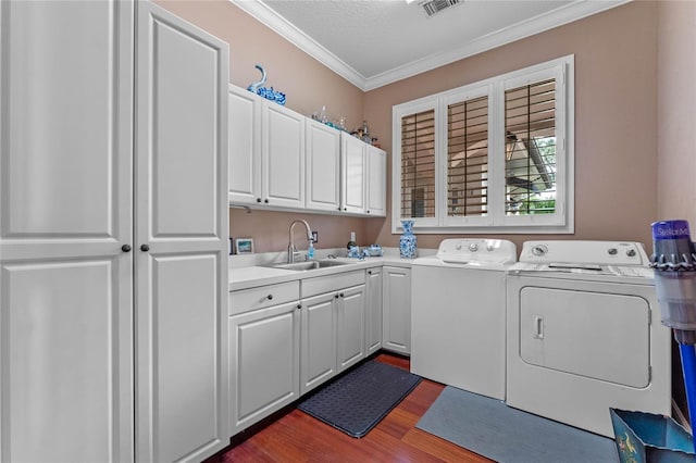 clothes washing area with washing machine and clothes dryer, sink, crown molding, cabinets, and hardwood / wood-style flooring