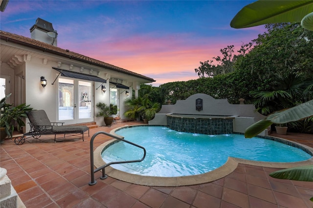 pool at dusk featuring a patio, pool water feature, and french doors