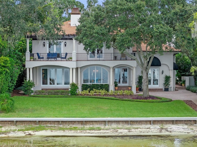 back of property featuring a lawn, a balcony, and a water view