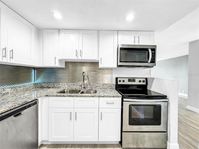 kitchen with light wood finished floors, light stone countertops, appliances with stainless steel finishes, white cabinetry, and a sink