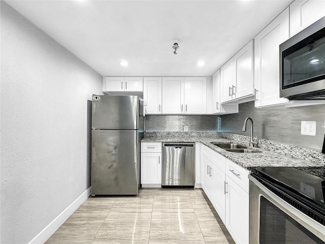 kitchen with light stone counters, a sink, stainless steel appliances, white cabinets, and tasteful backsplash