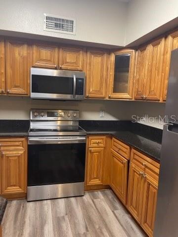 kitchen featuring dark stone countertops, light hardwood / wood-style floors, and appliances with stainless steel finishes