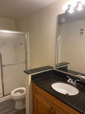 bathroom featuring a textured ceiling, wood-type flooring, toilet, a shower with shower door, and vanity