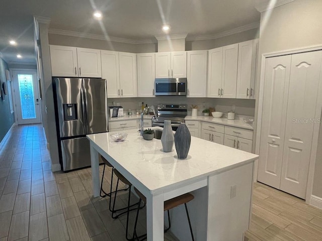 kitchen with a kitchen bar, sink, a center island with sink, stainless steel appliances, and white cabinets