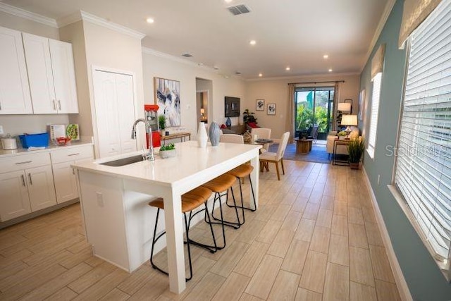 kitchen with an island with sink, sink, a breakfast bar area, white cabinets, and light hardwood / wood-style floors