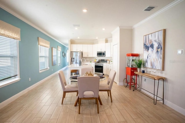 dining area with ornamental molding, sink, and light hardwood / wood-style floors