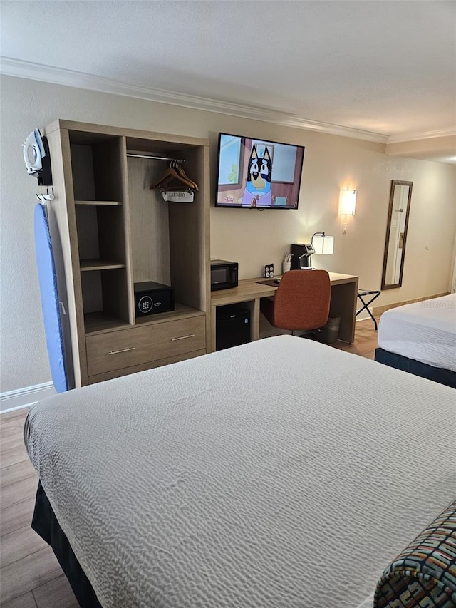 bedroom featuring ornamental molding, built in desk, a closet, and light wood-type flooring