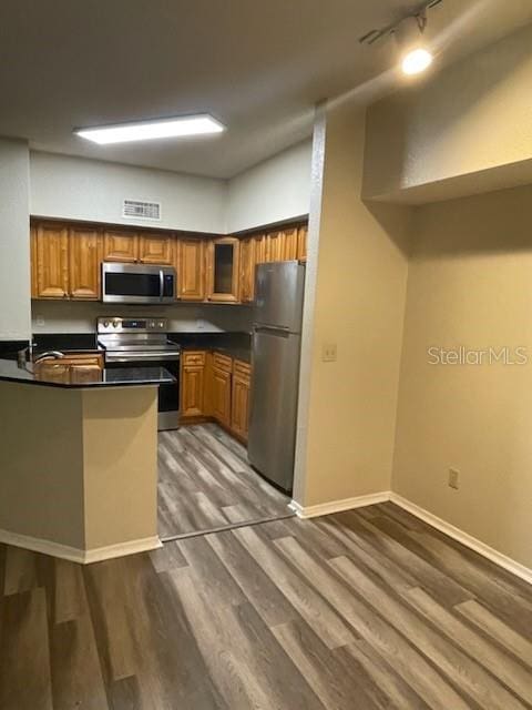 kitchen featuring rail lighting, stainless steel appliances, wood-type flooring, and kitchen peninsula