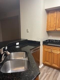 kitchen with light hardwood / wood-style floors, stainless steel dishwasher, sink, and dark stone counters