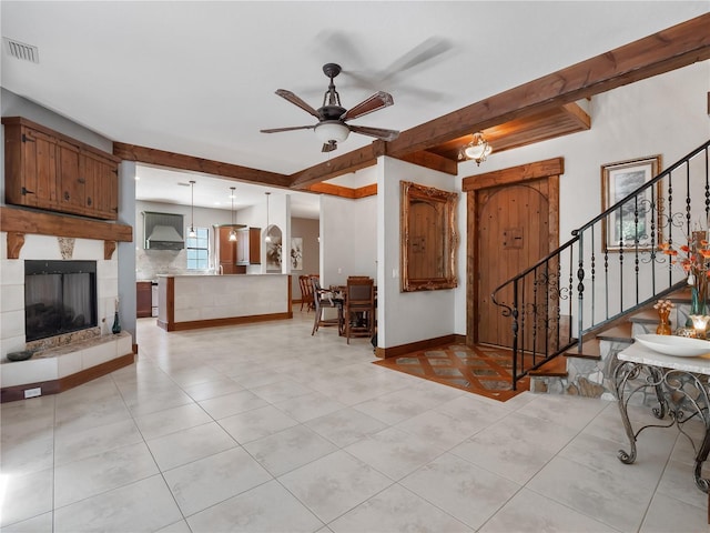 living room featuring ceiling fan with notable chandelier, beam ceiling, light tile patterned floors, and a tiled fireplace