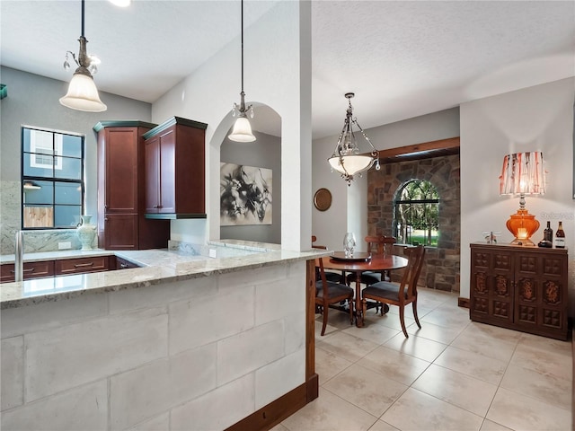 kitchen with hanging light fixtures, light stone counters, kitchen peninsula, a textured ceiling, and light tile patterned flooring