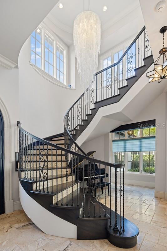 staircase with crown molding, an inviting chandelier, light tile floors, and a towering ceiling