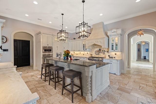 kitchen with an island with sink, backsplash, range, custom exhaust hood, and a kitchen bar