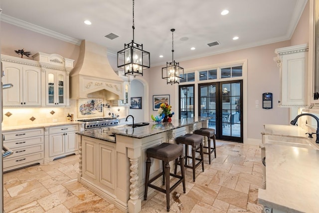 kitchen with backsplash, a kitchen bar, custom exhaust hood, a center island with sink, and pendant lighting