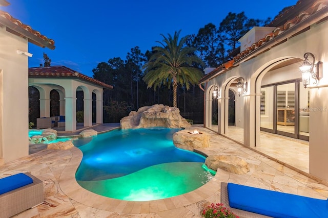 pool at twilight featuring pool water feature and a patio area