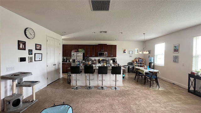 kitchen featuring light colored carpet, stainless steel appliances, a breakfast bar area, hanging light fixtures, and an inviting chandelier