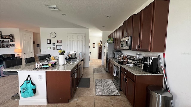 kitchen featuring a kitchen breakfast bar, light stone countertops, a center island with sink, appliances with stainless steel finishes, and light carpet