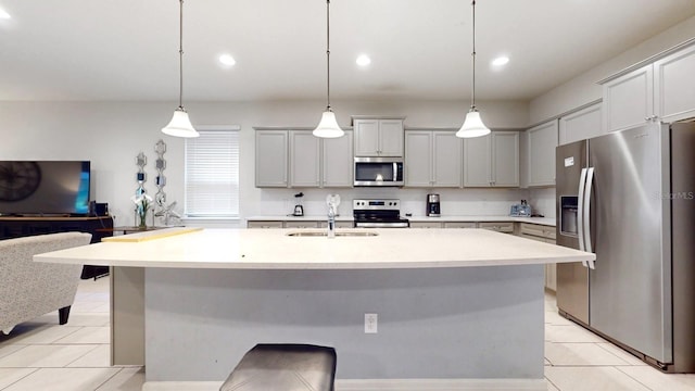 kitchen with an island with sink, stainless steel appliances, light tile flooring, hanging light fixtures, and sink