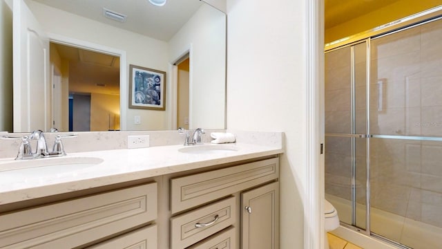 bathroom with a shower with shower door, toilet, and dual bowl vanity