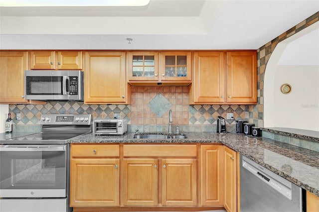 kitchen with dark stone countertops, appliances with stainless steel finishes, tasteful backsplash, and sink