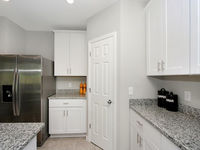 kitchen with white cabinetry, stainless steel fridge, light tile floors, and light stone countertops