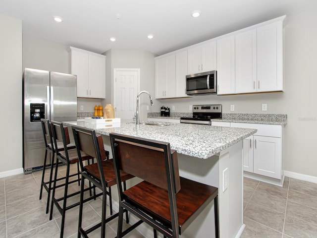 kitchen with a kitchen island with sink, a kitchen bar, white cabinets, light tile floors, and appliances with stainless steel finishes