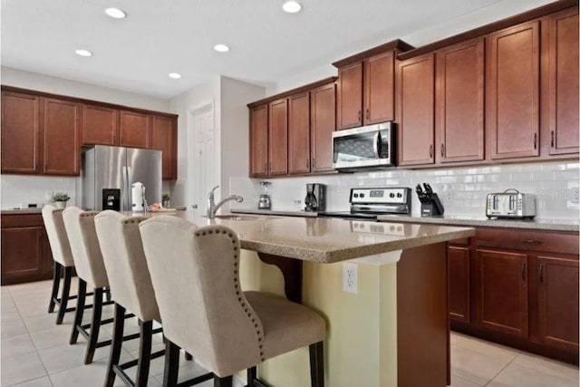 kitchen with a kitchen breakfast bar, appliances with stainless steel finishes, light tile patterned floors, and an island with sink