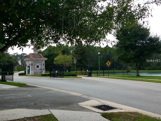 view of road featuring curbs, a gated entry, traffic signs, and sidewalks