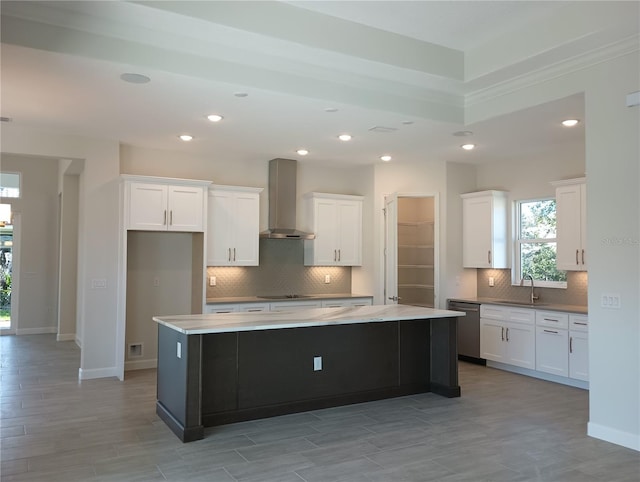 kitchen featuring stainless steel dishwasher, white cabinets, a sink, a kitchen island, and wall chimney range hood