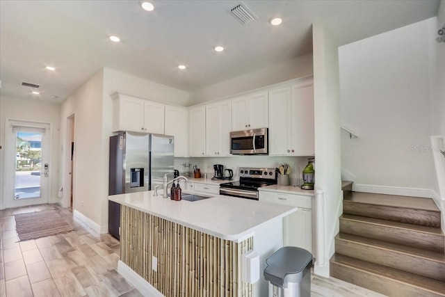 kitchen featuring a center island with sink, appliances with stainless steel finishes, white cabinetry, light wood-type flooring, and sink