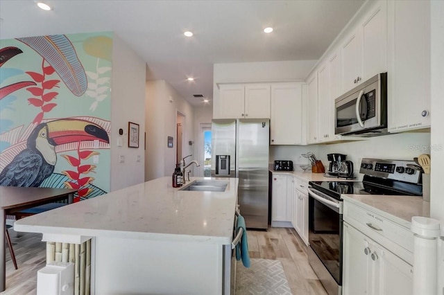 kitchen featuring stainless steel appliances, white cabinets, sink, and light hardwood / wood-style flooring