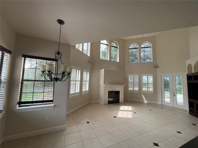 unfurnished living room with an inviting chandelier, a wealth of natural light, light tile flooring, and french doors