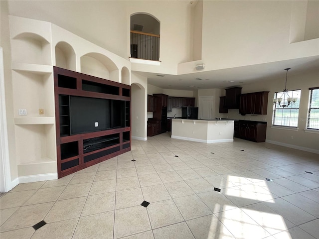 unfurnished living room with light tile floors, a notable chandelier, a high ceiling, and built in shelves