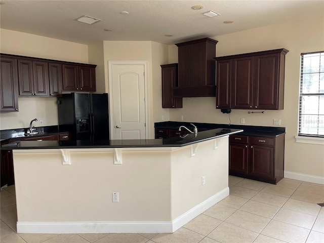 kitchen with a kitchen breakfast bar, black fridge with ice dispenser, custom range hood, light tile flooring, and dark brown cabinetry