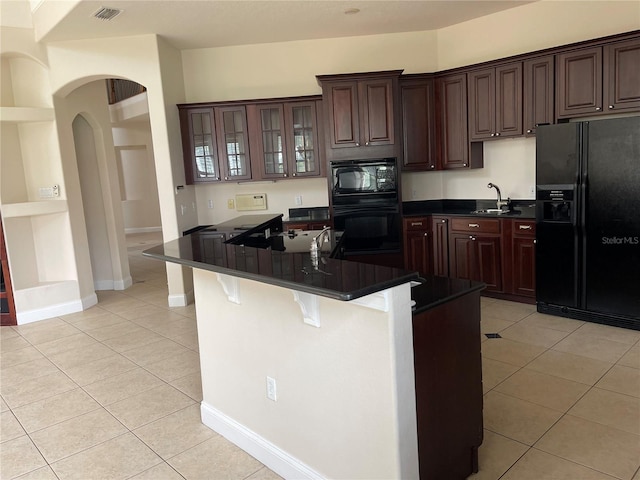 kitchen with sink, light tile floors, a breakfast bar area, black appliances, and dark brown cabinetry