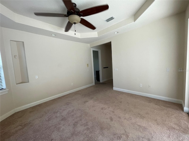 empty room featuring ceiling fan, a raised ceiling, and light colored carpet