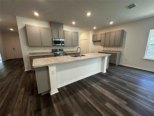 kitchen featuring sink, dark wood-type flooring, appliances with stainless steel finishes, gray cabinetry, and an island with sink