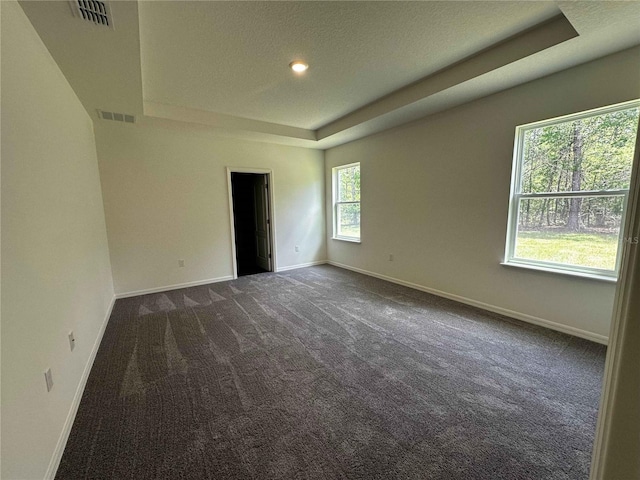 empty room featuring dark colored carpet, a textured ceiling, and a tray ceiling