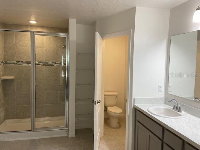 bathroom with a shower with shower door, vanity, toilet, tile patterned floors, and a textured ceiling