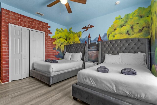 bedroom with a closet, brick wall, light hardwood / wood-style floors, and ceiling fan